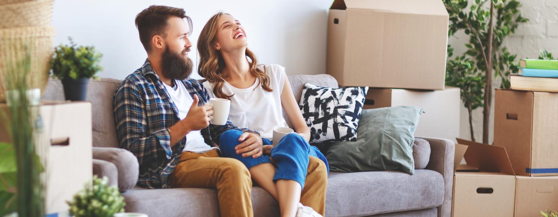 a man and a woman sitting on a couch with boxes and a coffee cup
